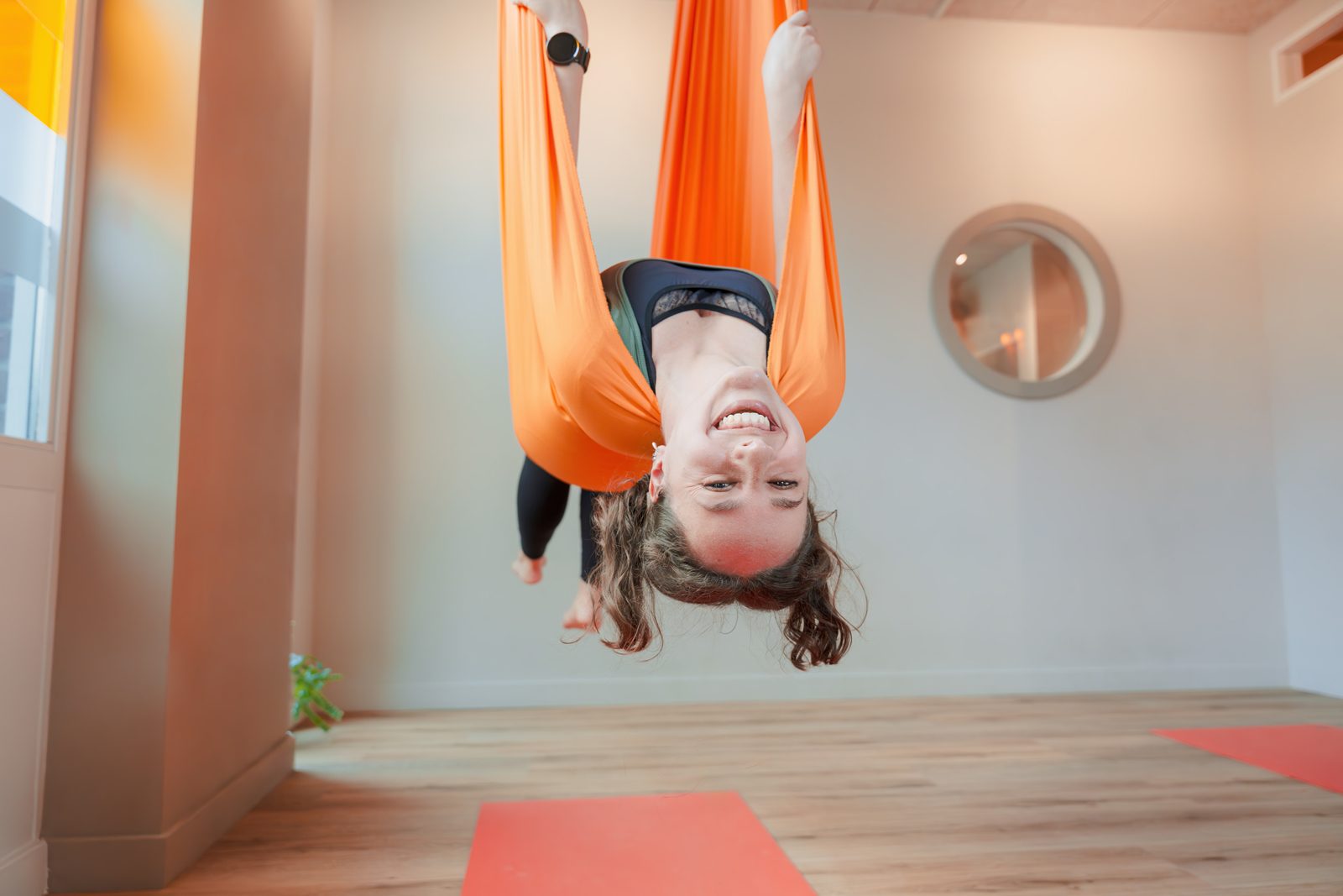 Aerial yoga: cursist hangt ondersteboven in een oranje hangmat